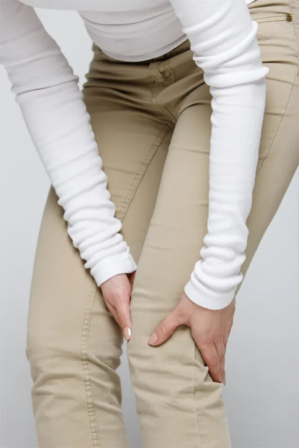 A woman living in Miami wearing a white long-sleeve shirt and tan pants, clutching her knee, suffering from arthritis.