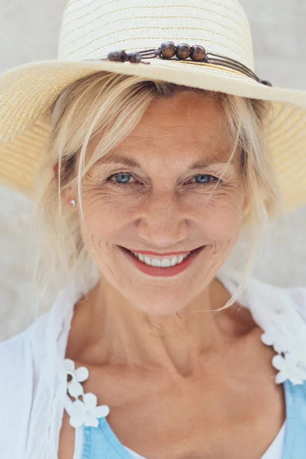 A beautiful, smiling older woman with blonde hair and a sunhat, living with menopause in Miami.