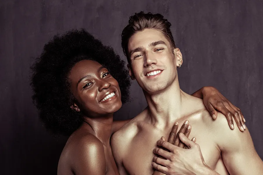 Miami-Face-and-Skin-Doctor A beautiful black woman and white man stand with arms around each other against a gray background, happy with face and skin treatments from Vida Integrative Health of Miami in Miami.