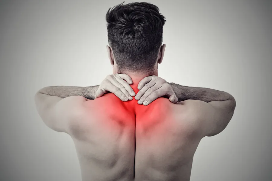 A shirtless man is seen from the back rubbing his shoulders and neck with his hands. The image is black and white except for a red area around the source of the pain. He needs care for fibromyalgia from Vida Integrative Health of Miami in Miami.