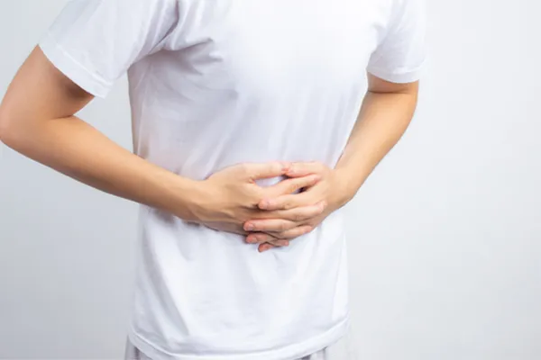 A man in a white t-shirt holds his stomach in pain from digestive issues. Get treated for proper Gut Health from Vida Integrative Health of Miami in Miami.