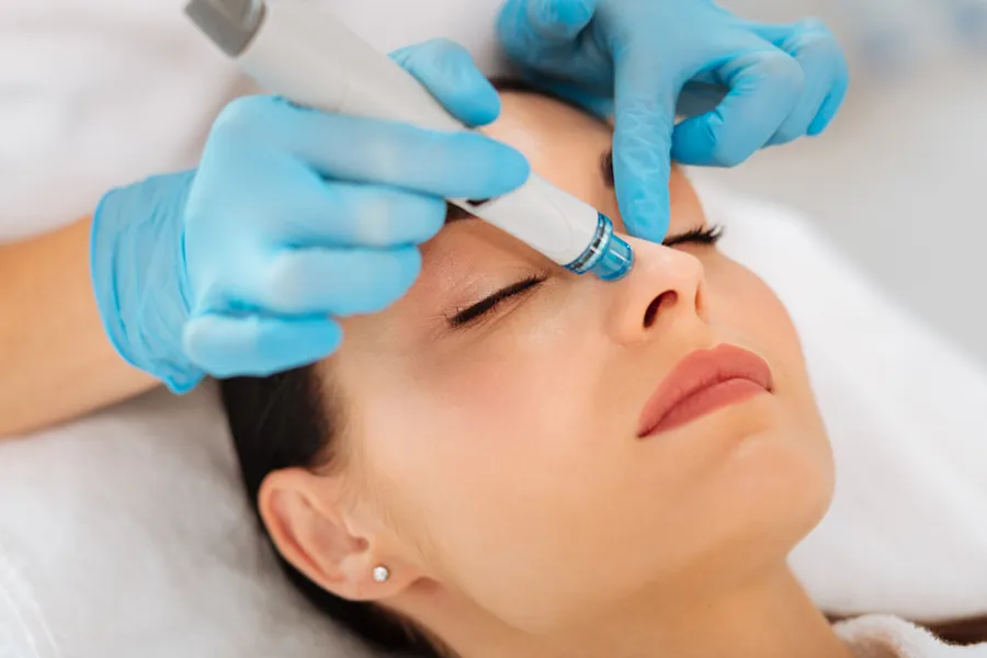A woman in towels lies down receiving a HydraFacial treatment from Vida Integrative Health of Miami in Miami.
