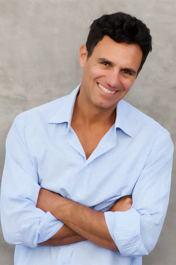 A man in a light blue button-up shirt standing against a gray wall and smiling due to the success of intense pulse light therapy from Vida Integrative Health of Miami in Miami.