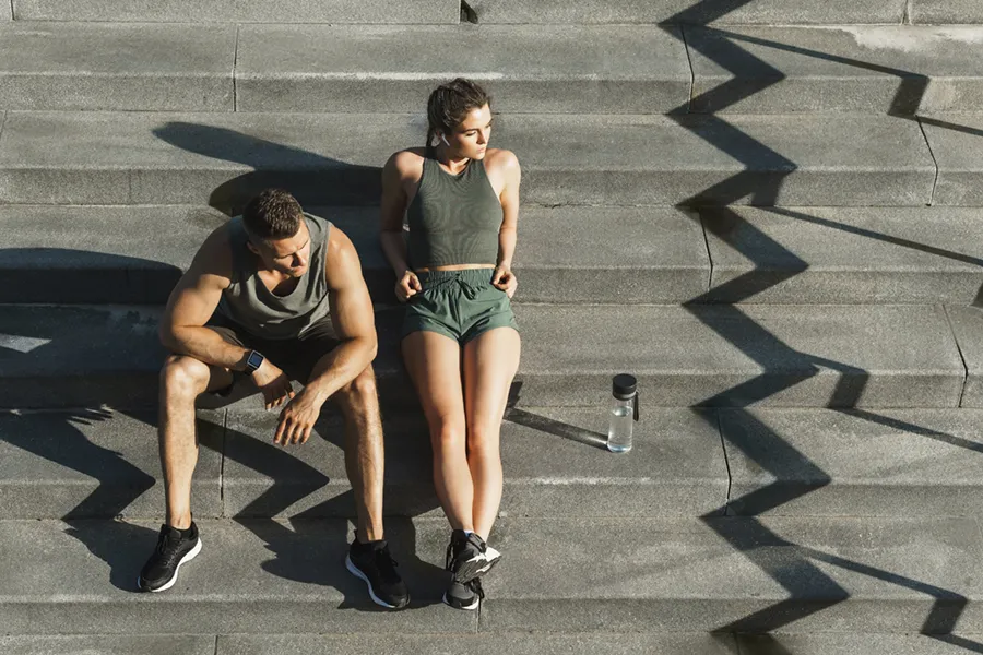 A couple in gray and green track clothes resting after a workout on stone steps, happy with their weight loss plans from Vida Integrative Health of Miami in Miami.