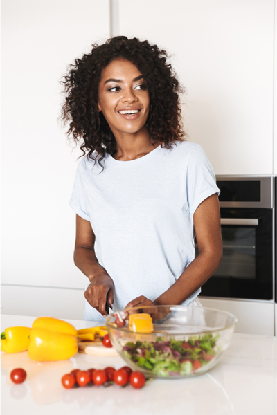 A woman in a white t-shirt prepares a vibrant, healthy salad in her kitchen, signifying nutraceutical services from Vida Integrative Health of Miami in Miami.