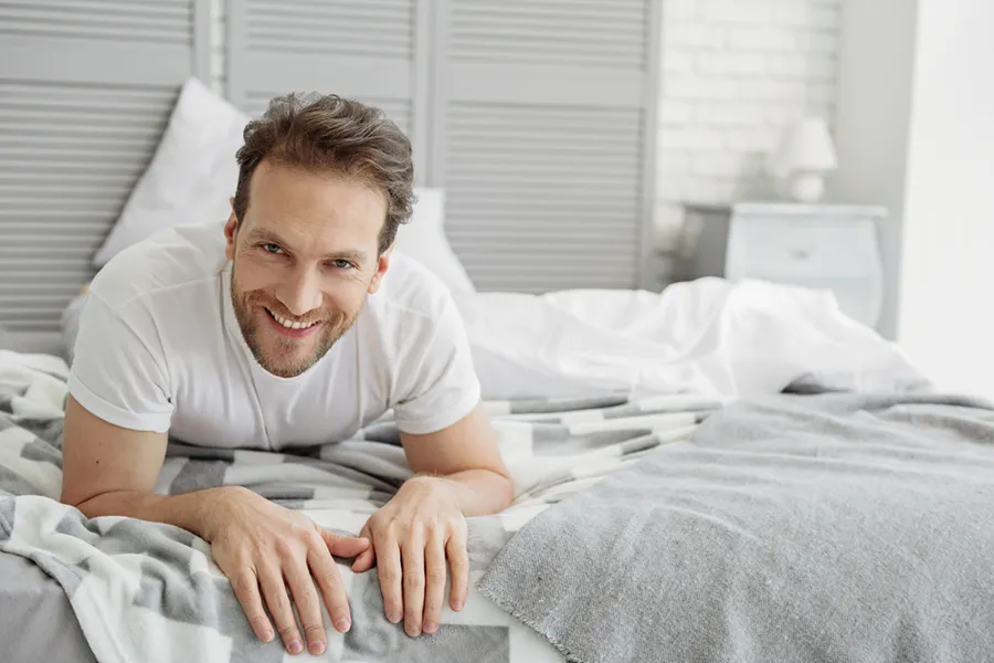 A man lying on his stomach on a bed and smiling, signifying sexual wellness care from Vida Integrative Health of Miami in Miami.