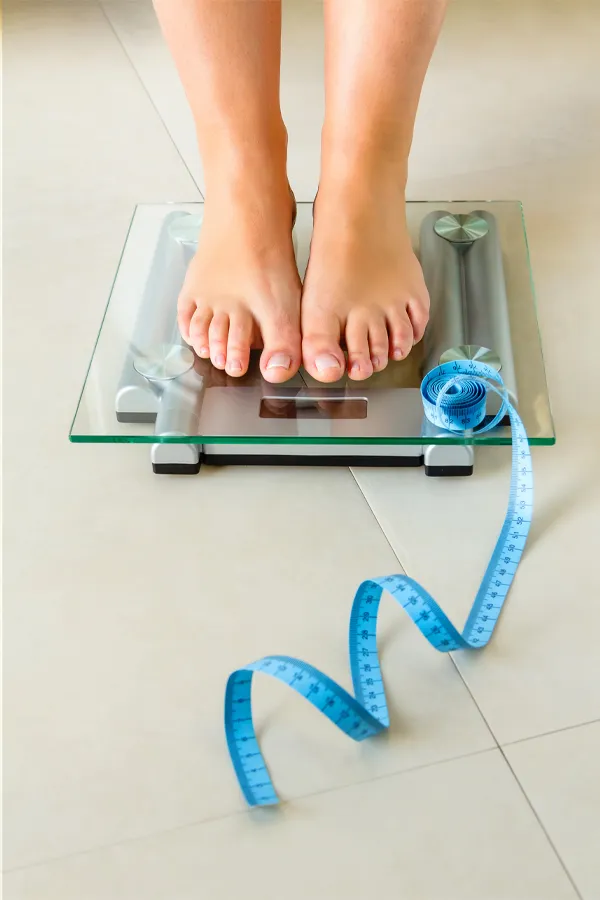 Close-up of a woman's feet in Miami standing on a scale, with measuring tape by her toes, getting treatment for weight loss resistance.